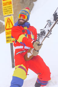 Man in vintage ski suit holding ski and snowboard, embodying 80s nostalgia.