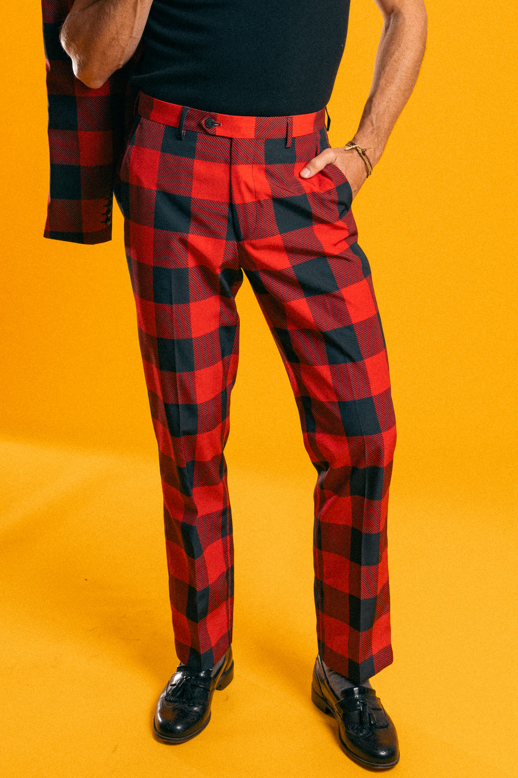 A person in The Red & Black Lumberjack | Buffalo Check Plaid Suit Pants with a close-up of black shoe and bracelet.