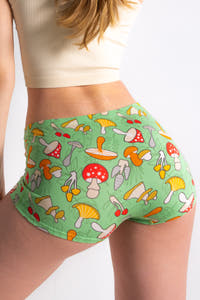 A whimsical woman wears The Trip Advisor | Mushroom Modal Boyshort Underwear, embodying Shinesty's playful fashion vibe with mushroom patterned green shorts.