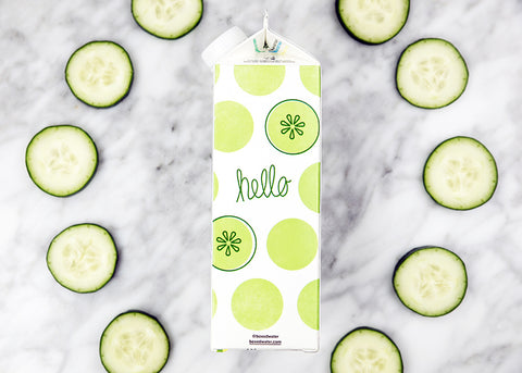 carton with cucumber pattern surrounded by real cucumber slices