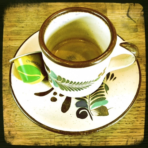 A small ceramic espresso cup sits on a ceramic saucer on a wooden table.