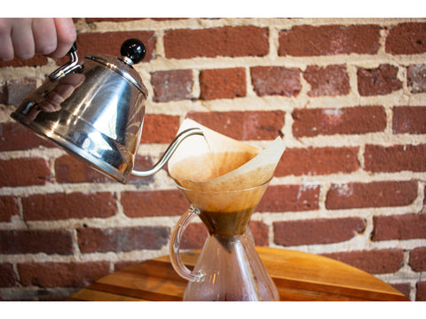 Chemex Coffee Maker, with a filter and coffee, being filled with hot water.