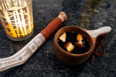 A cup of black coffee served in a mug carved out of a birch burl, with cheese curds floating atop.