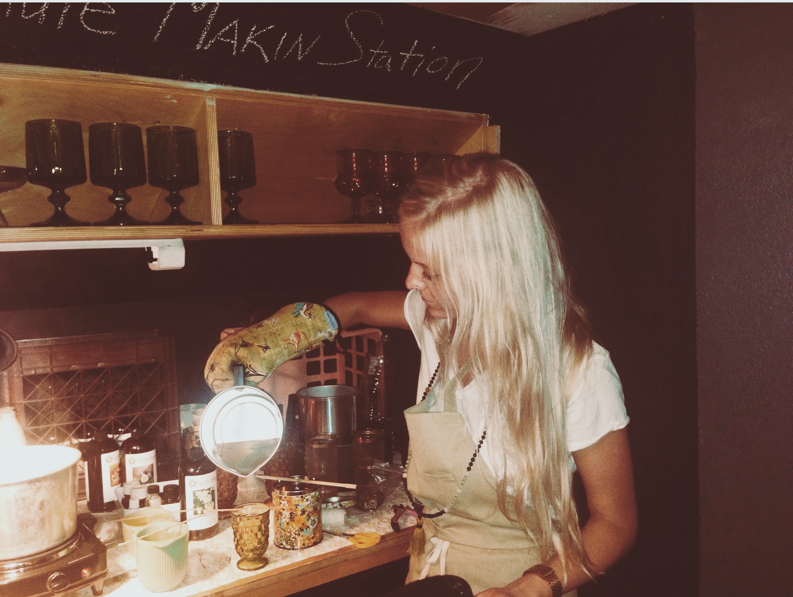 Circa 2014 my first lil candle studio in a closet. A picture of me pouring candles from metal pitcher, with the words "candle makin station" written in chalk above me.