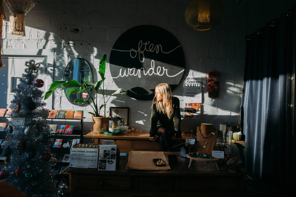 sarah sits in the san diego shop in front of the large logo on the wall