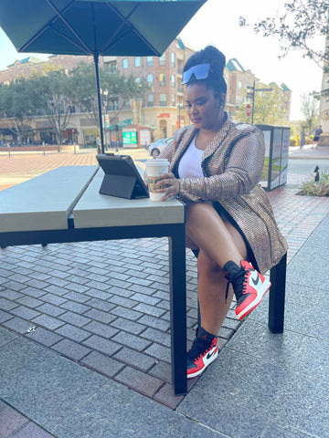 Morgan B. working on her IPad wearing a gold metallic blazer and red, white, and black Jordan One sneakers