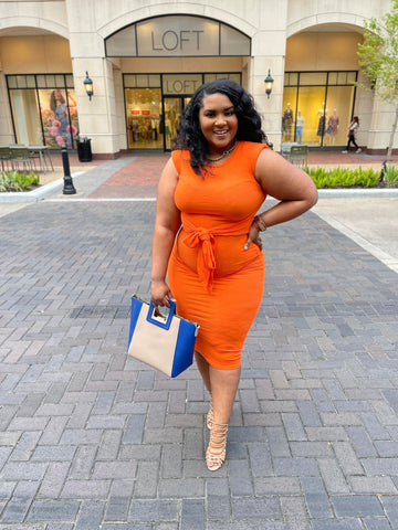 Morgan B. wearing a sleeveless orange tie around the waist dress with a color block nude and blue purse 