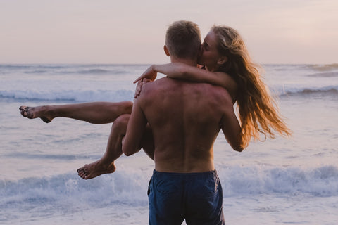 Back view of man holding woman beside waves