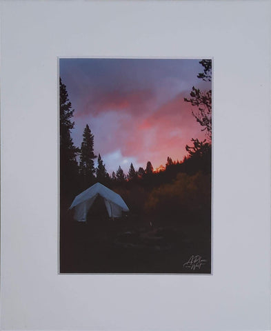 Mountain sunset with a white tent and pine trees surrounding.