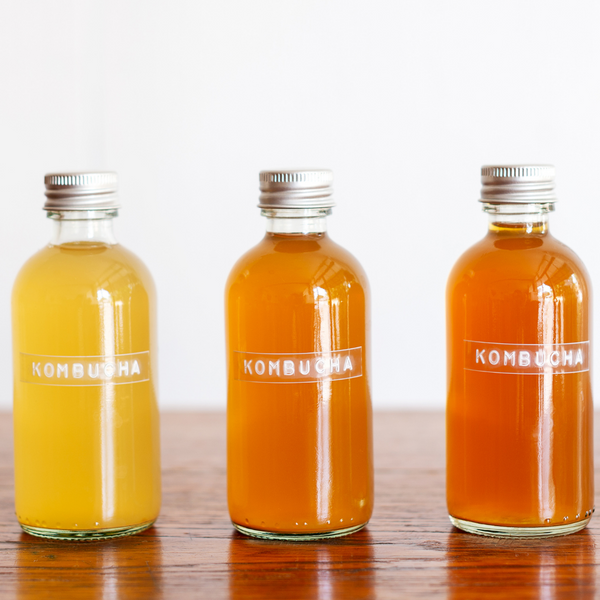 what is kombucha? three bottles of kombucha in a row on a wood counter with a white background