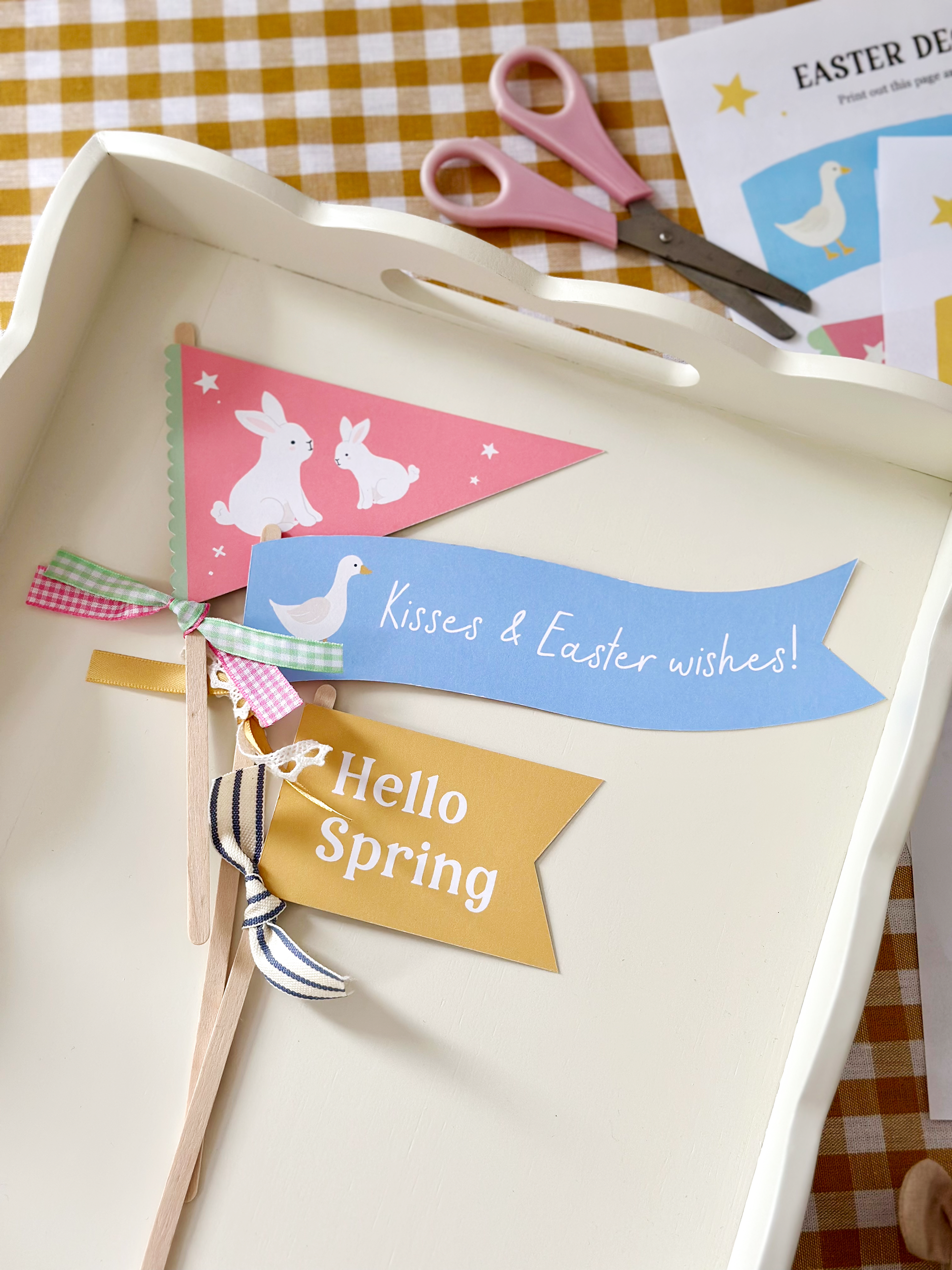 A collection of pastel coloured Easter flags made from card, each featuring cheerful designs and festive text. The flags are neatly arranged on a white wooden tray, creating a charming and playful Easter display perfect for seasonal decorating or party inspiration.