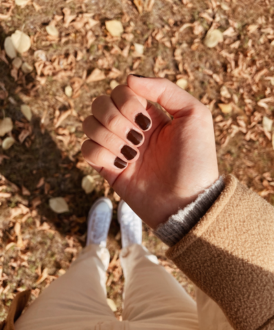 Fall brown nails in front of autum leaves sitting on the ground