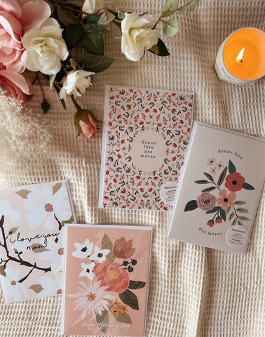 Greeting Mother's Day Cards From Mimi & August layed on a bed with flowers and a candle burning beside them