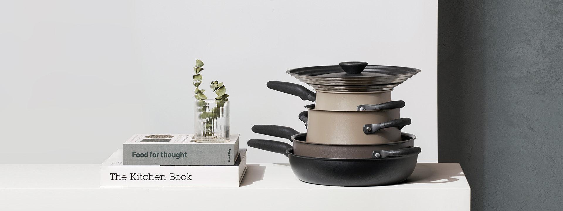 Meyer Cookware Cinder and Smoke cookware set displayed on white table with books and vase