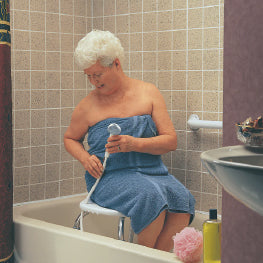 An elderly woman using a hand-held shower spray in a bathtub