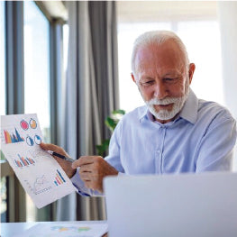 An elderly man holding up a financial document while on a computer