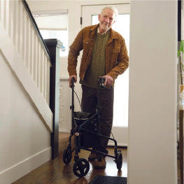 An elderly man using a three wheeled rollator in his home