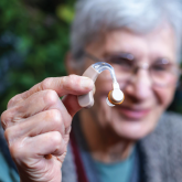 An elderly woman holding up a hearing aid
