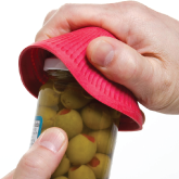 A person using a jar opener to open a jar of olives