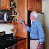 An elderly man using a reacher grabber to grab items in a cabinet