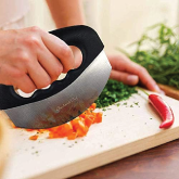 A person using a rocker knife to cut vegetables in a kitchen