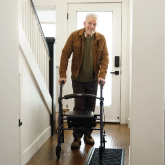 An elderly man walking with a rollator in his home