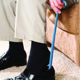 An elderly man putting on his shoes using a shoe horn