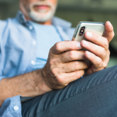 An elderly man sitting down looking at his smart phone