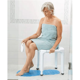 An elderly woman sitting on a bath mat using a hand-held shower spray