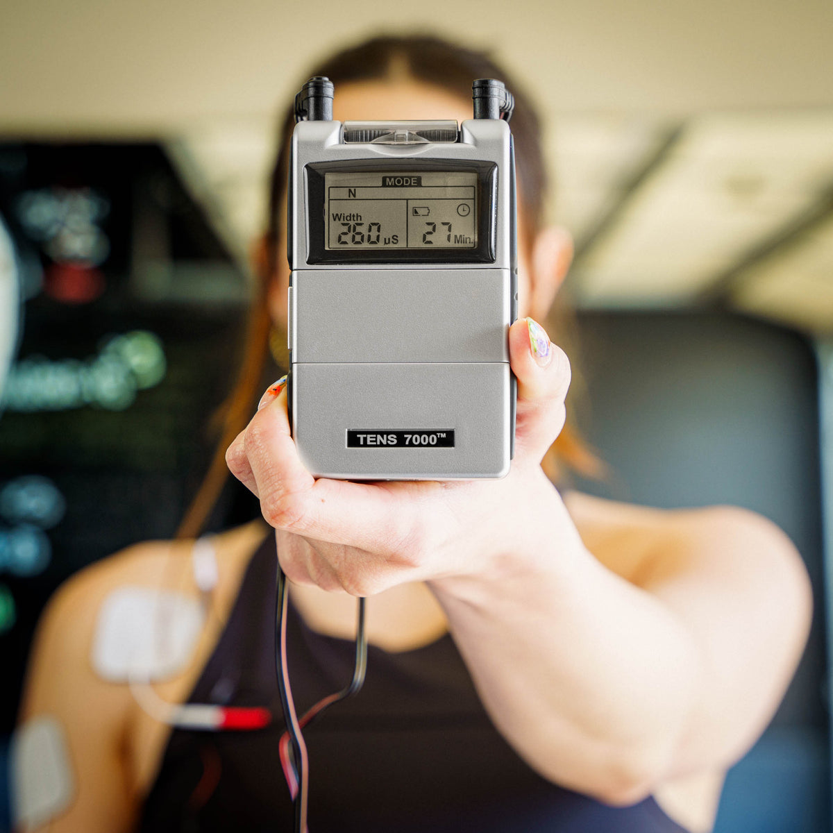 A close up of the TENS 7000 Rechargeable TENS Unit being held with a blurry background