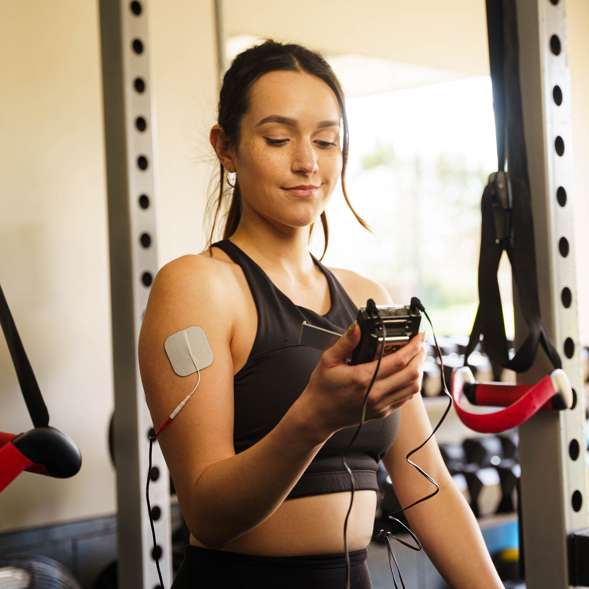 A woman holding the TENS and EMS combo unit in a gym