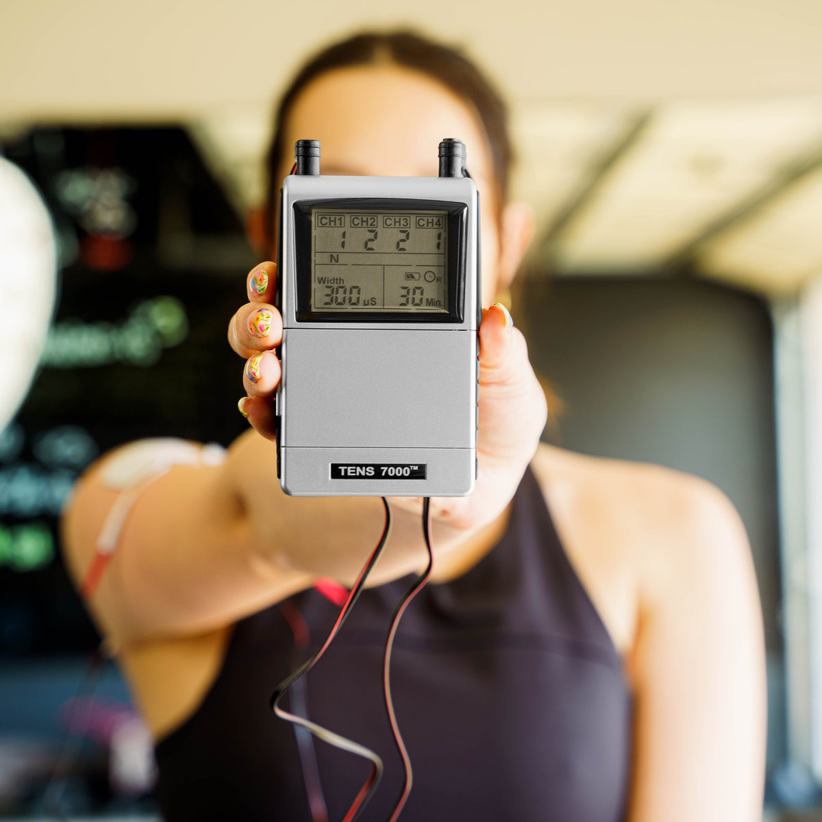 A woman holding the TENS and EMS combo unit up close