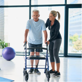 An elderly man using a walker with a physical therapist supporting him