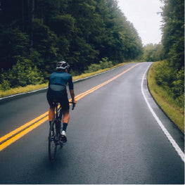 A man biking on a street through a forest