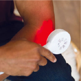 Close up of a red light therapy device being used on a man’s elbow