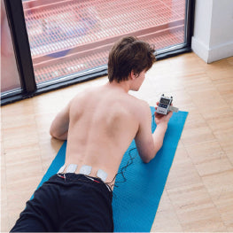 A man using a TENS unit on his hip while on a yoga mat