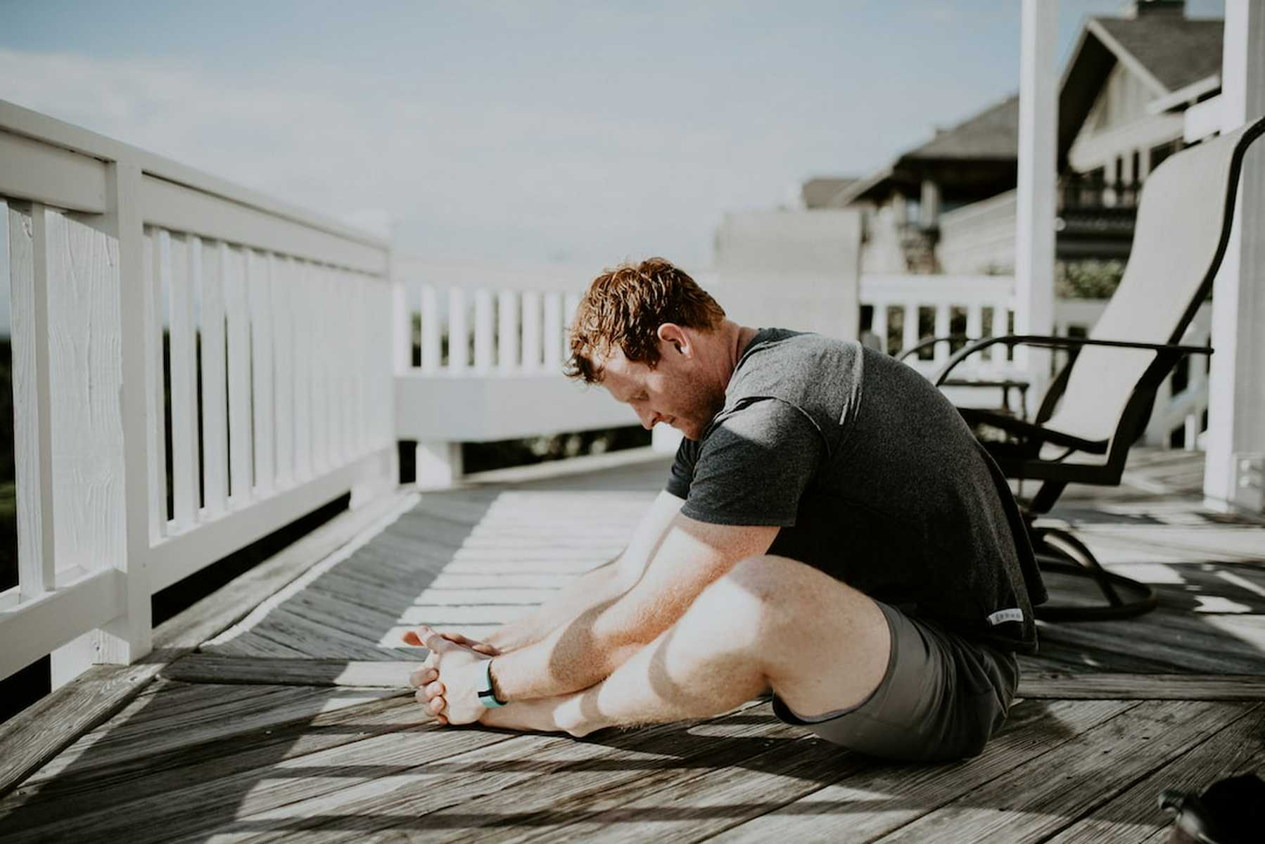 A man sitting on a deck outside stretching his hip flexor