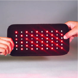 A red light therapy device being held by two hands