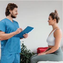 A doctor holding a clipboard talking to a patient sitting on a bed