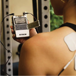 A woman holding a TENS unit with electrodes on her back