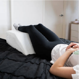 A wedge pillow being used at the end of a bed