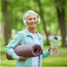 A senior woman with headphones, a yoga mat, and a water bottle