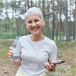 A senior woman with headphones on and a water bottle in her hand