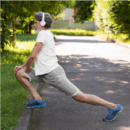 An elderly man stretching with headphones on