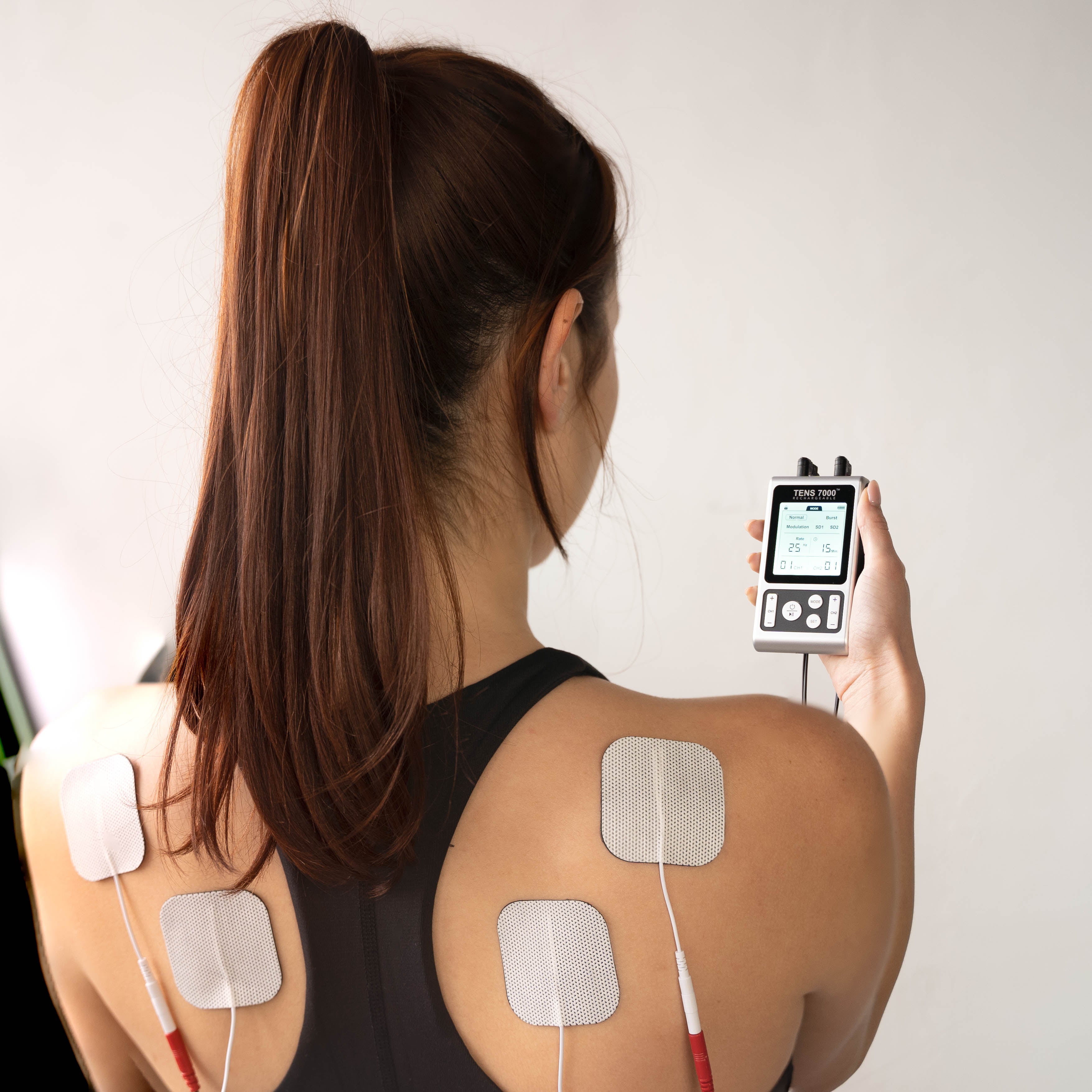A woman standing away with a TENS unit and pads on her back