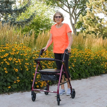 A woman walking on a sidewalk outside while using the Care Rolling Walker