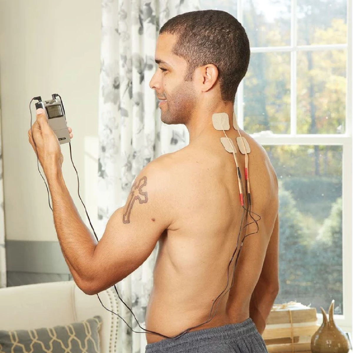 A shirtless male using the TENS 7000 2nd Edition TENS unit on the back of his neck