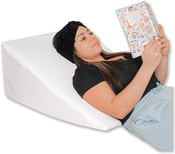 A woman laying on a wedge pillow while reading a book