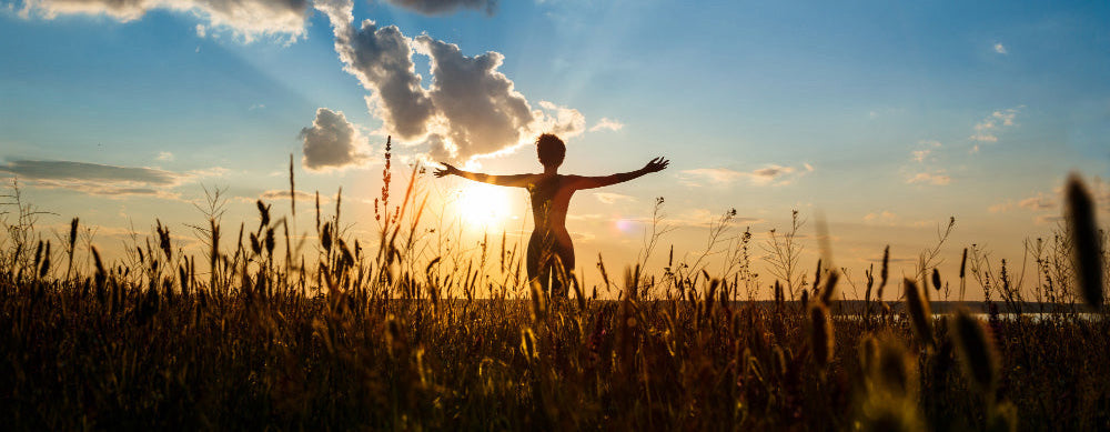 A woman holding her hands out in a field in front of sunlight.