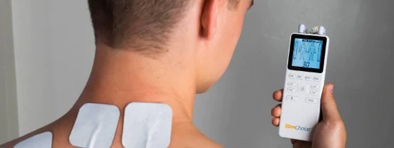 A male holding a TENS unit up with electrodes on his back